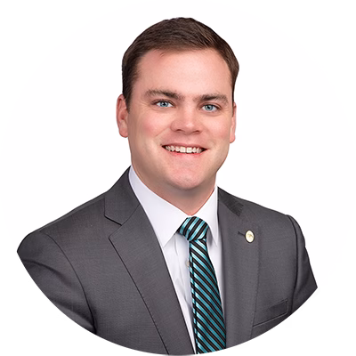 A young man in a gray suit, white shirt, and striped tie smiles at the camera against a plain white background.