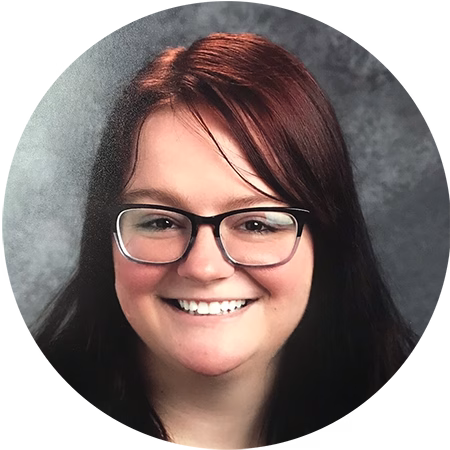 A woman with straight, dark brown hair and glasses smiles at the camera against a gray, textured background.