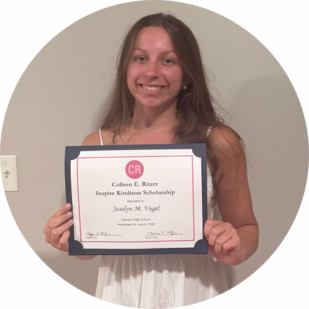 Young woman with long brown hair wearing a white sleeveless dress, smiling and holding a certificate for the Colleen E. Ritzer Inspire Kindness Scholarship awarded to Josselyn M. Vogel.